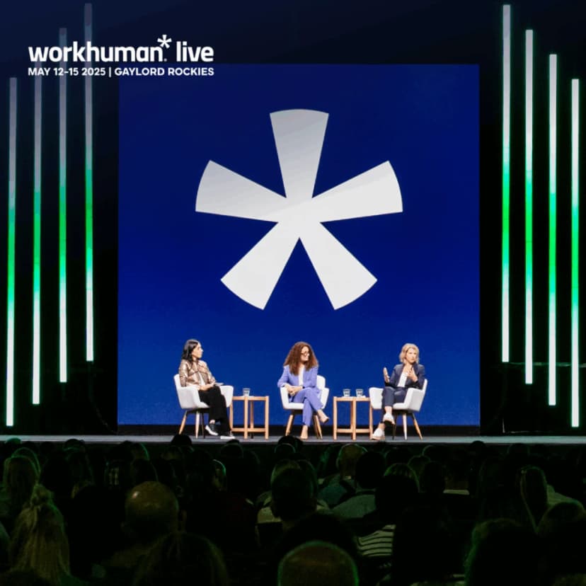 A panel discussion at the Workhuman Live event features three speakers seated on stage, with a large blue backdrop displaying a prominent asterisk logo. The audience is visible in the foreground, engaged with the presentation. The event details, including the date and location, are displayed at the top of the image.