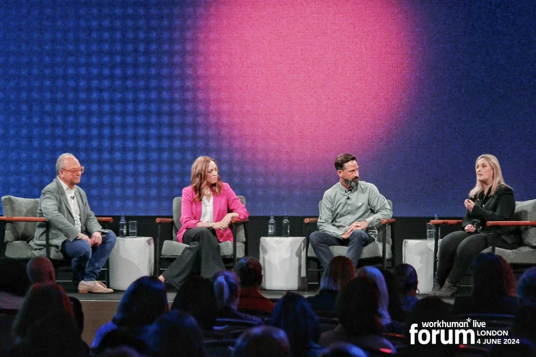 A panel of four speakers engaged in discussion during the Workhuman Live event in London. The setting includes a softly lit background with a gradient design, and the speakers are seated in modern chairs on stage. The audience is visible in the foreground, attentively listening.