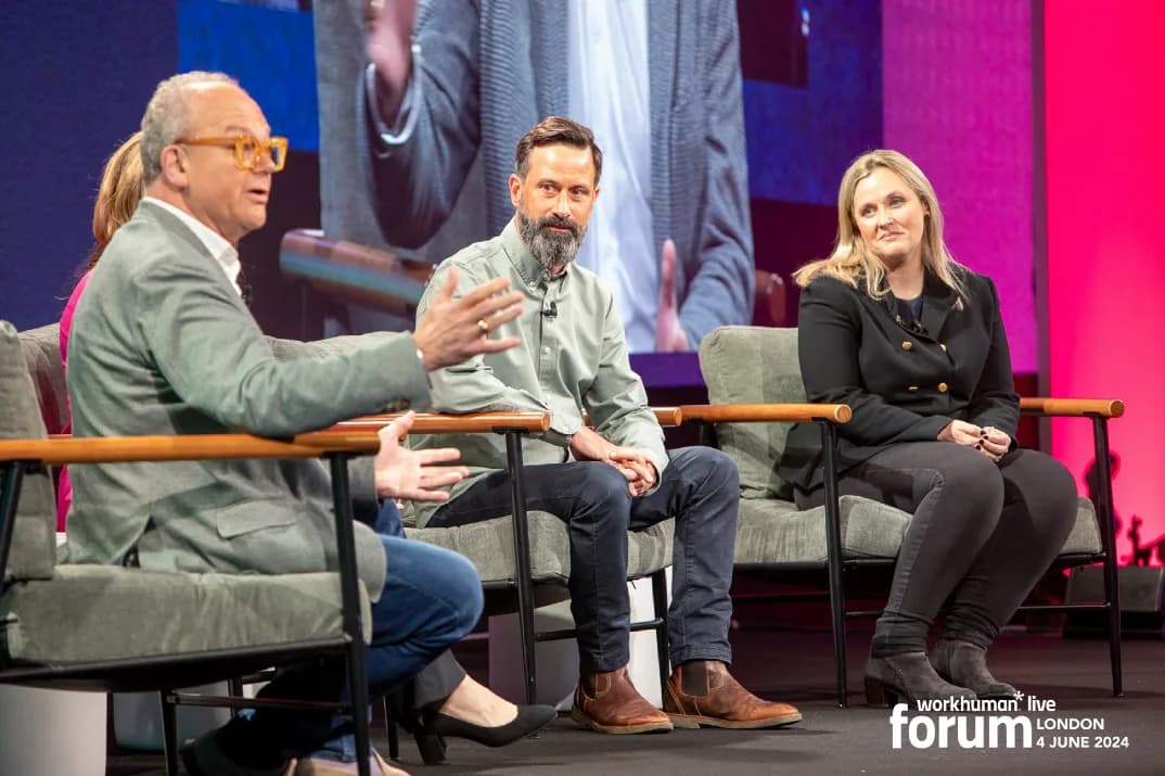 A panel discussion at the Workhuman Live Forum features four speakers seated onstage. One speaker, wearing glasses and a gray blazer, gestures while speaking. The others, including a man with a beard in a green shirt and a woman in a black jacket, listen intently.