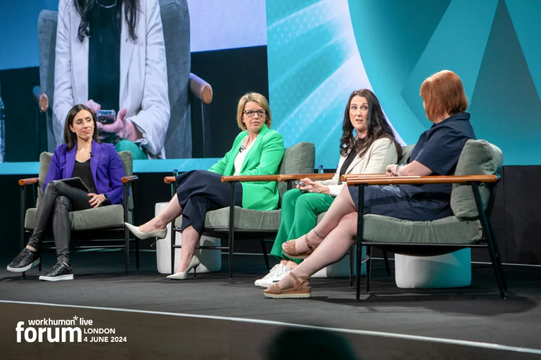 A panel of four women speakers are seated on stage at the Workhuman Live Forum in London. They engage in discussion, with one speaker holding a device and gesturing, while the others listen attentively.