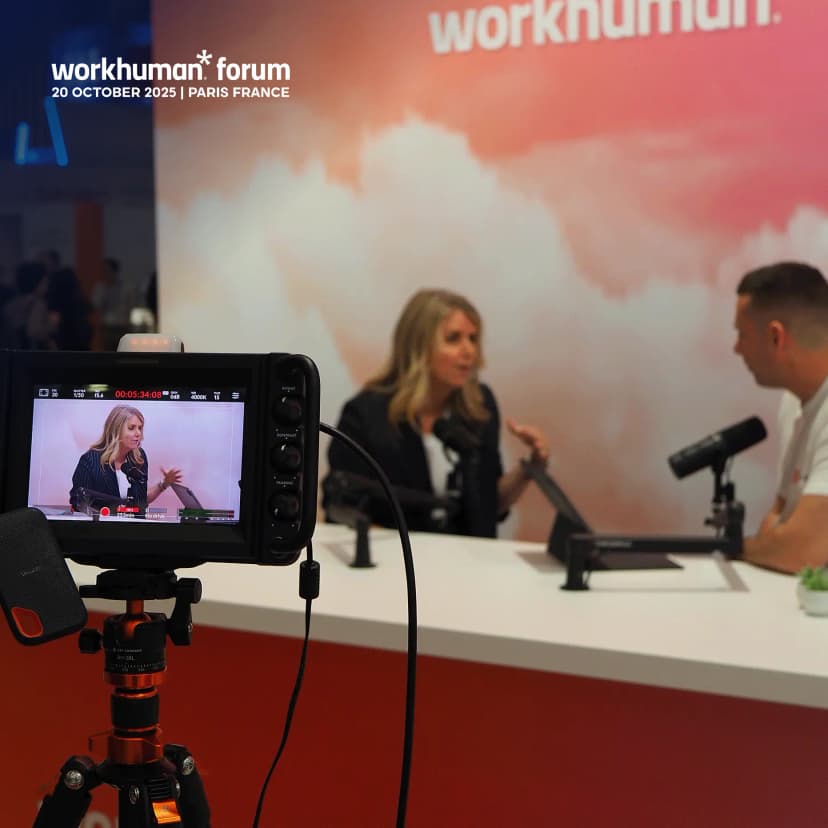 A camera is focused on a woman with blonde hair speaking passionately during a discussion at the Workhuman Forum event. The background features a gradient design with the Workhuman logo and text indicating the event's date and location: "20 OCTOBER 2025 | PARIS FRANCE." Another person is seated across from her, actively engaging in the conversation. Microphones are set up in front of both speakers, emphasizing the interview or panel format.