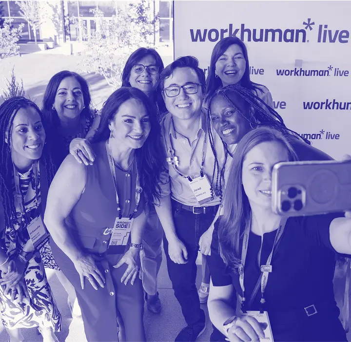 A group selfie featuring eight smiling individuals at the Workhuman Live event, with a backdrop displaying the Workhuman Live logo. The attendees are wearing name badges and are standing together, exuding a sense of camaraderie. The image captures the energy and excitement of the conference atmosphere.