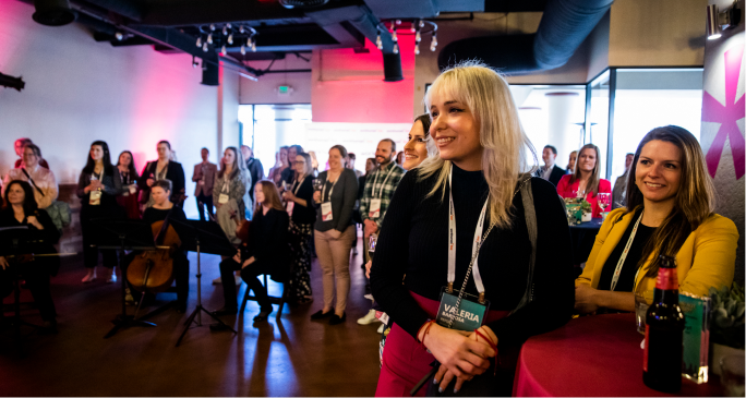 A group of attendees at a Workhuman event stands together in a spacious room with a modern aesthetic. The focus is on a woman with blonde hair, smiling and wearing a black outfit, with a name badge visible that reads 